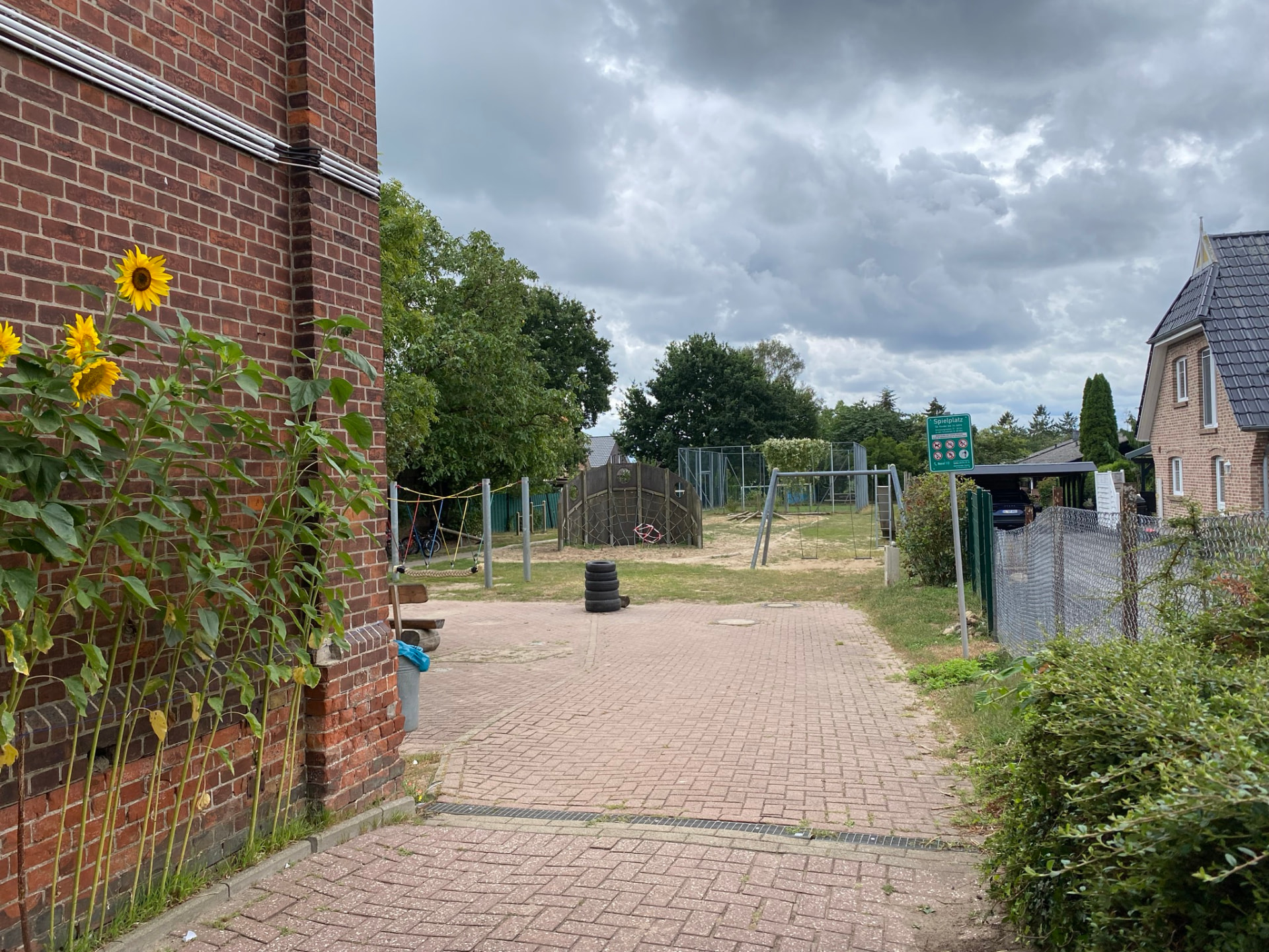 Blick vom Schulgebäude über den gepflasterten Hof zum Spielplatz, Sonnenblumen an der Backsteinwand